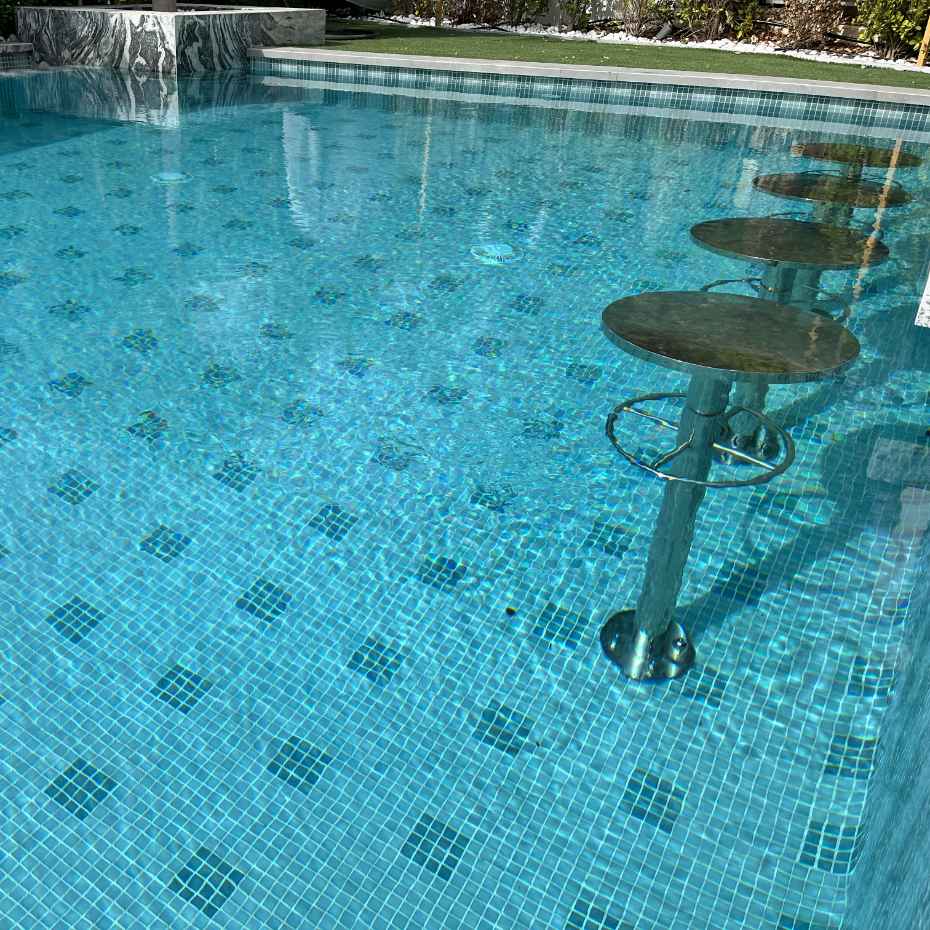 Diagonal View Of A Swimming Pool Adorned With EGM-201 Light Green Glass Mosaic Pool Tiles And Seating Stools.