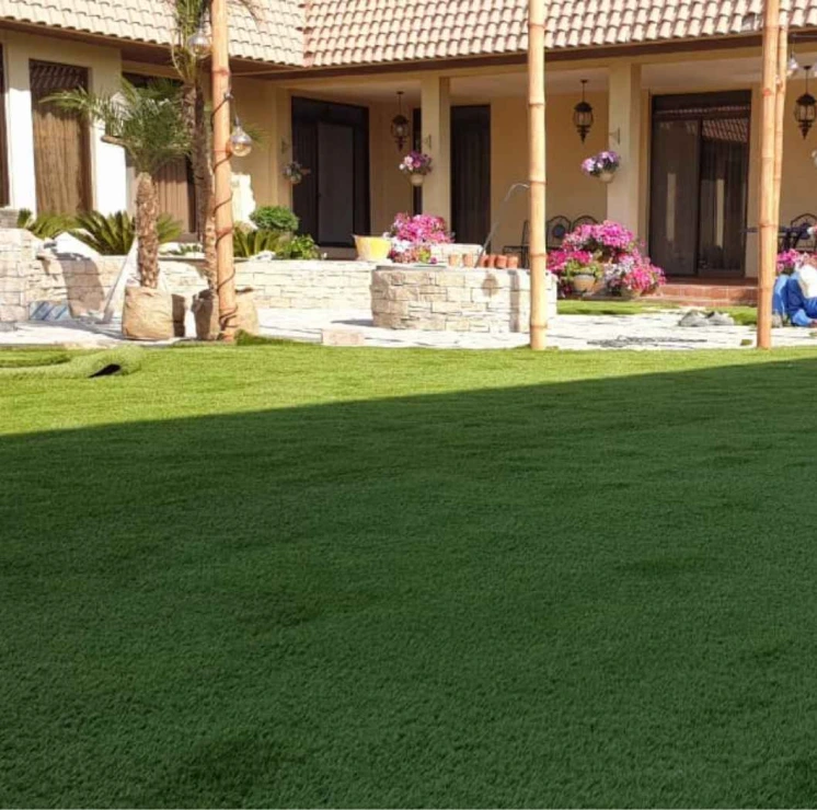 Beautiful villa garden with Elixir artificial grass Dubai, surrounded by flowers, palm trees, and stone landscaping.