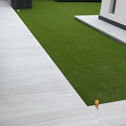 Modern home exterior with white tiled flooring surrounding a neatly installed fake grass yard.