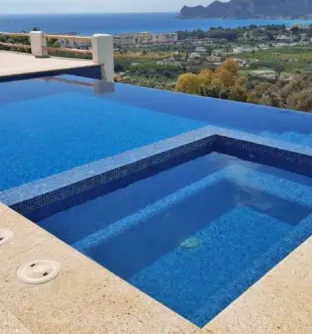Hillside infinity pool overlooking coastline, finished with deep blue swimming pool tiles mosaic