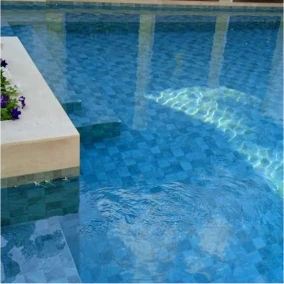 Clear swimming pool water reflecting sunlight with mosaic tile for a pool and built-in planter.